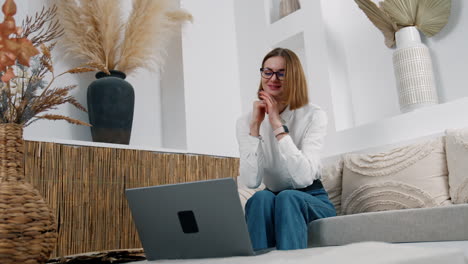 smiling positive woman sits at the opened laptop. lady waves her hand to the camera having video chat online. low angle view.
