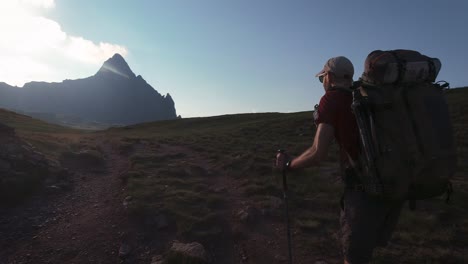 Vista-Trasera-De-Un-Excursionista-Con-Una-Gran-Mochila-Caminando-Hacia-El-Pico-De-La-Montaña-En-La-Soleada-Puesta-De-Sol-De-La-Tarde-En-Verano