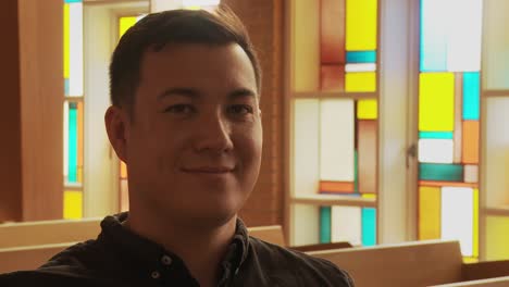 close up of a young ethnic man smiling into the camera while sitting inside a church sanctuary