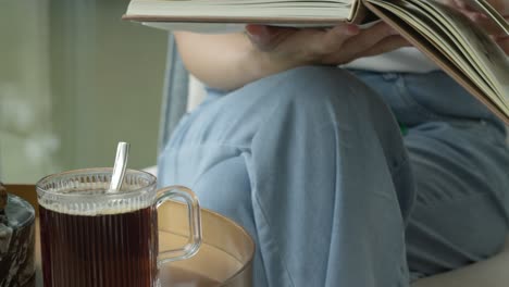 Woman-reading-a-book-on-a-tea-break,-sitting-on-a-chair-relaxing