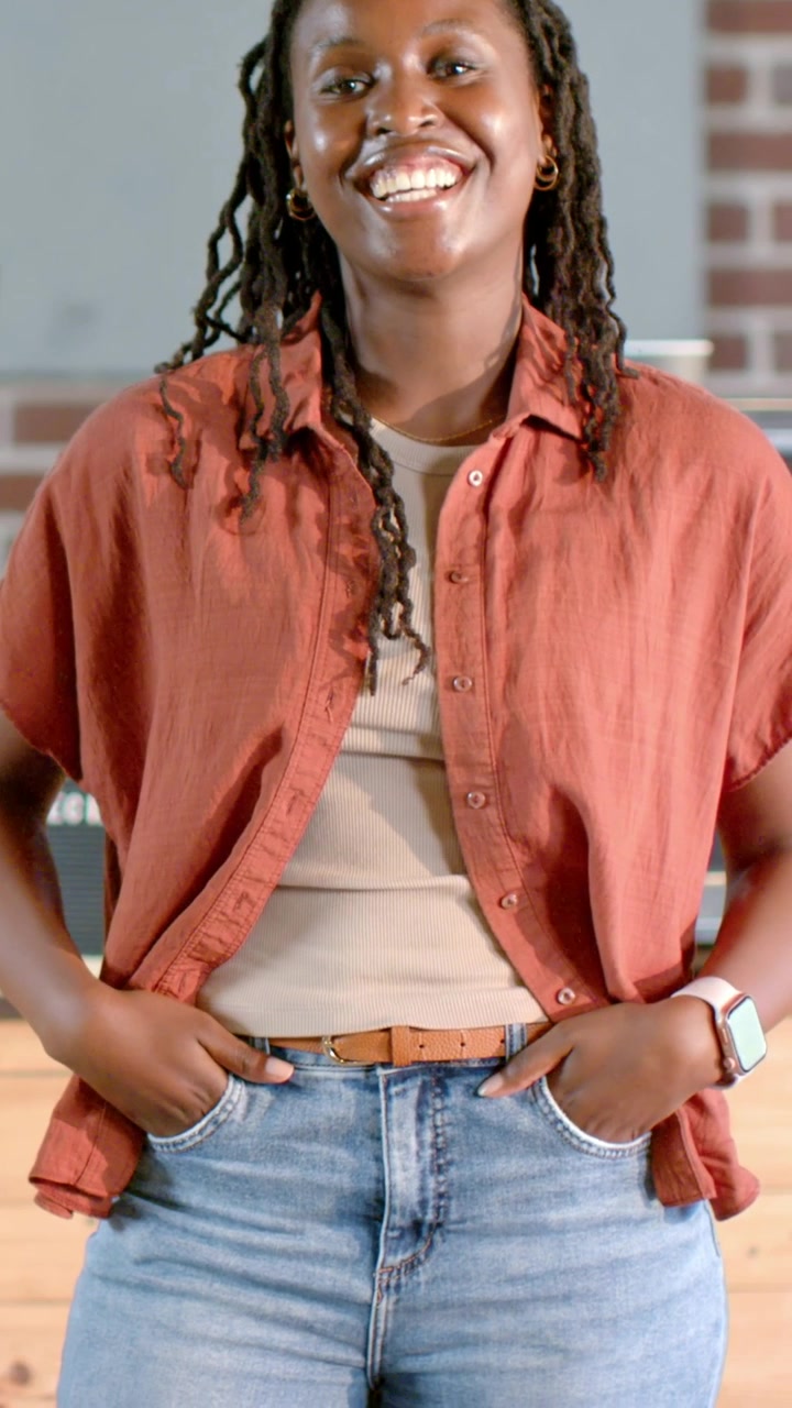 Vertical video: Smiling adult woman in rust shirt and jeans, shifting head into laughter at counter