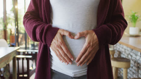 midsection of caucasian pregnant woman gesturing heart over belly