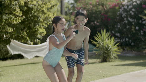 two children jumping in swimming pool, holding action camera.