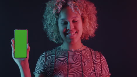 young woman holding smartphone with green screen in neon light