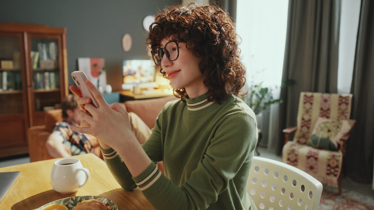 Young Woman Checking Social Medial on Phone and Smiling at Home
