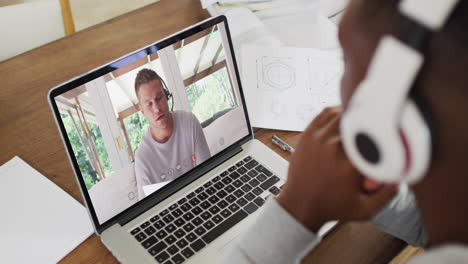 hombre de negocios afroamericano sentado en un escritorio usando una computadora portátil haciendo una videollamada con un colega masculino