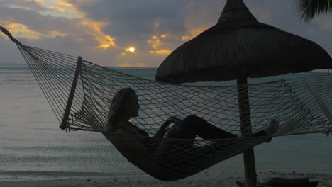 woman relaxing in hammock on beach and taking cell photos