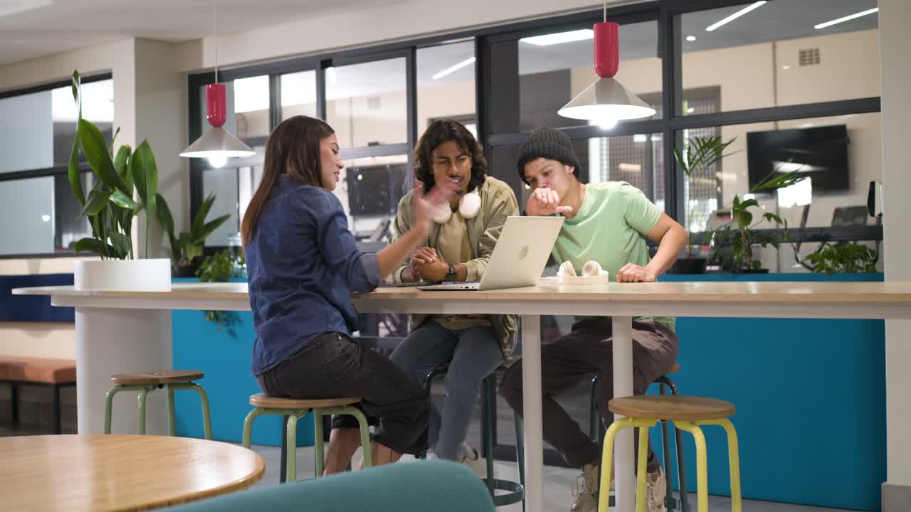 African American coworkers leaning in, woman picking up earbuds, reviewing laptop for work at table