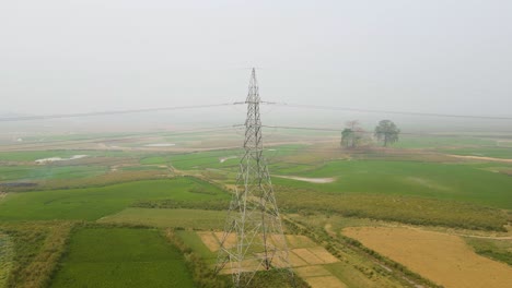 a zoom-out shot from a high-voltage power pylon in a foggy rural landscape, showcasing the industrialization of countryside and the scale of our energy infrastructure