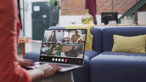 Biracial woman using laptop for video call, with diverse business colleagues on screen