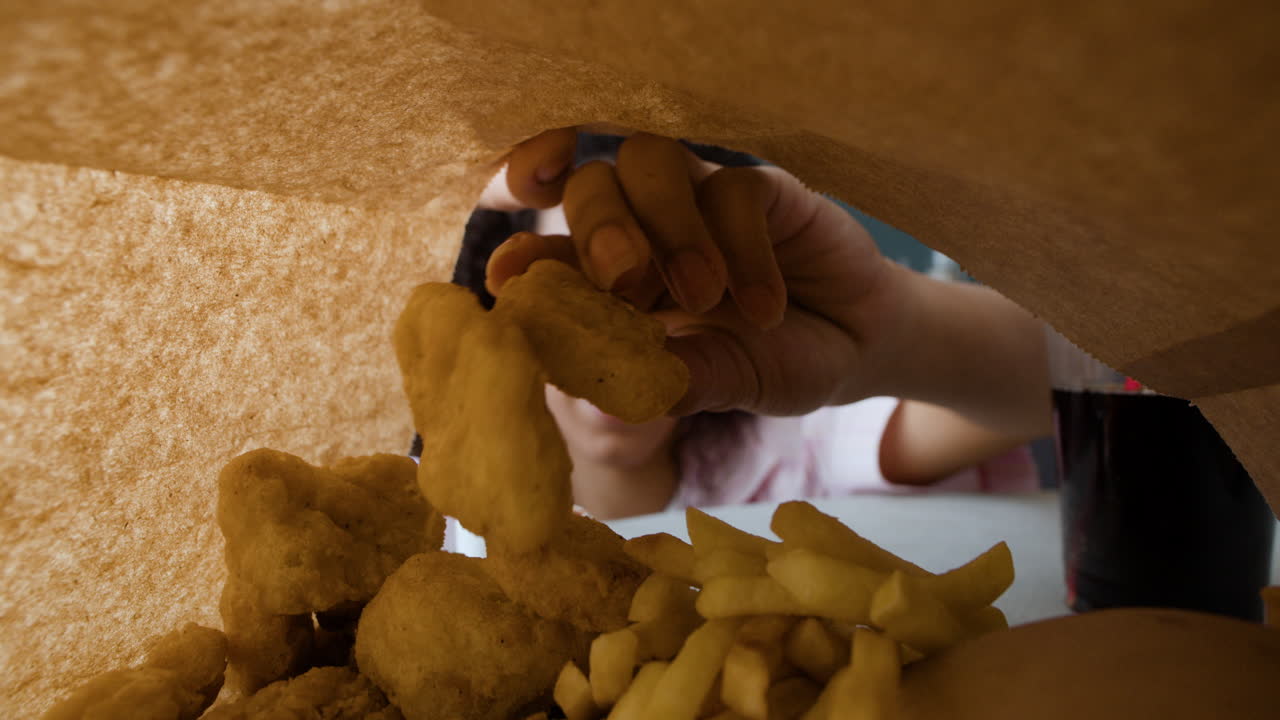 A person's hand reaches into a paper bag filled with chicken nuggets and french fries.