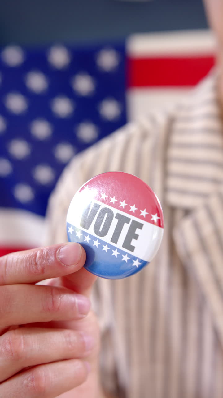 Vertical video of hand of biracial man holding american flag badge with vote text, slow motion