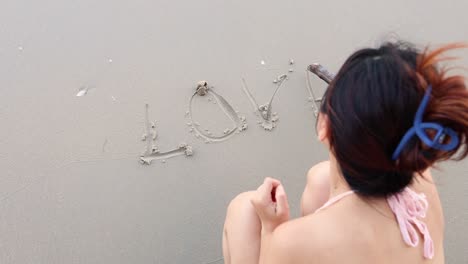 person inscribing 'love' on the beach sand