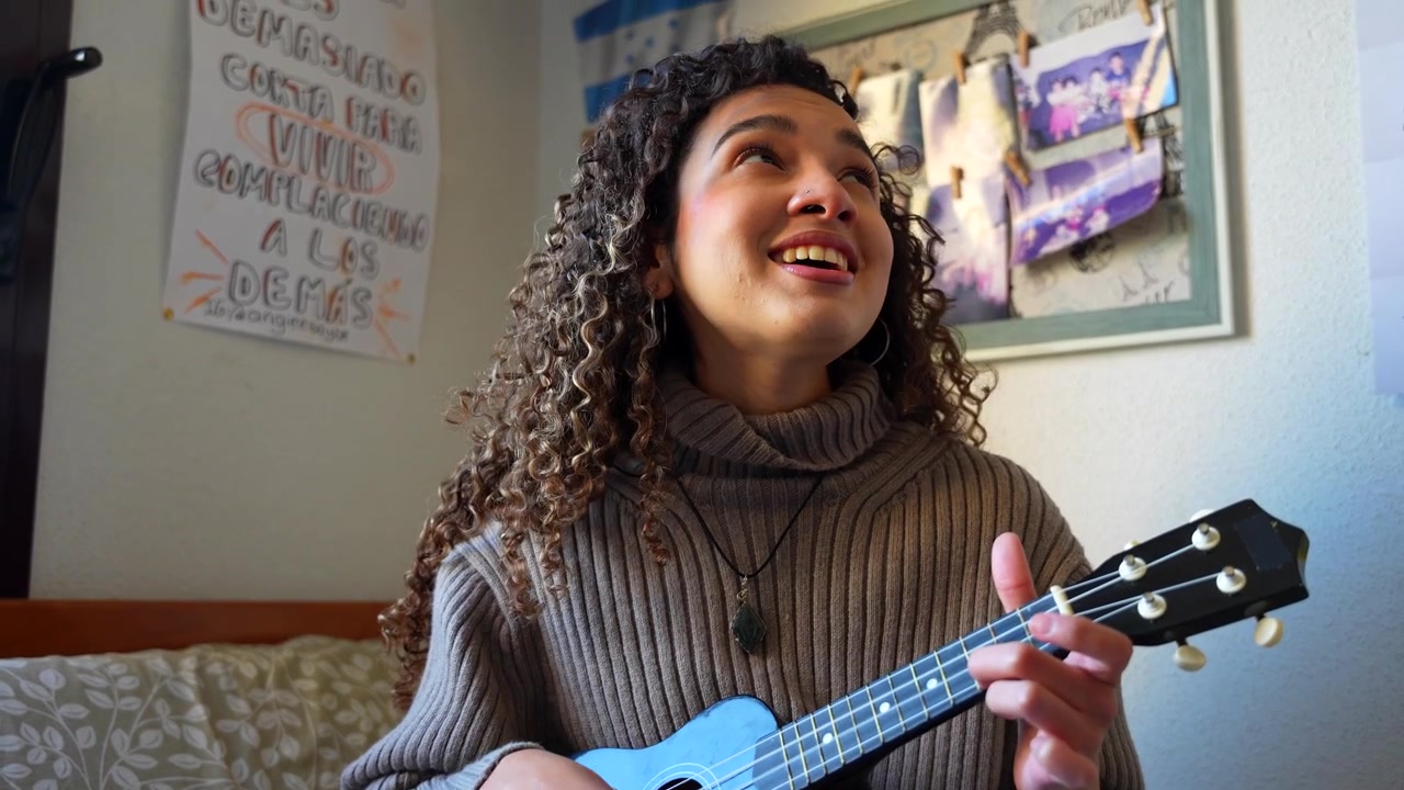 Curly haired female musician enjoying her hobby, singing and playing a ukulele at home