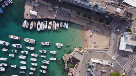 Kleiner-Strand,-Umgeben-Von-Einer-Stadt-Mit-Vielen-Booten-Und-Einzelpersonen,-Die-Schwimmen-Gehen