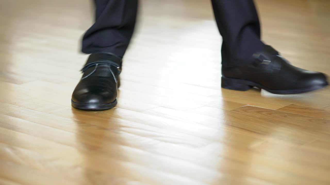 Legs of a man in black shoes dancing elements of dubstep on the brown floor background. View shot looking straight at the shoes and legs in black trousers.