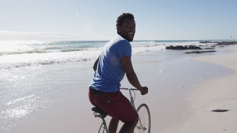 Hombre-Afroamericano-Sonriendo-Y-Andando-En-Bicicleta-En-La-Playa