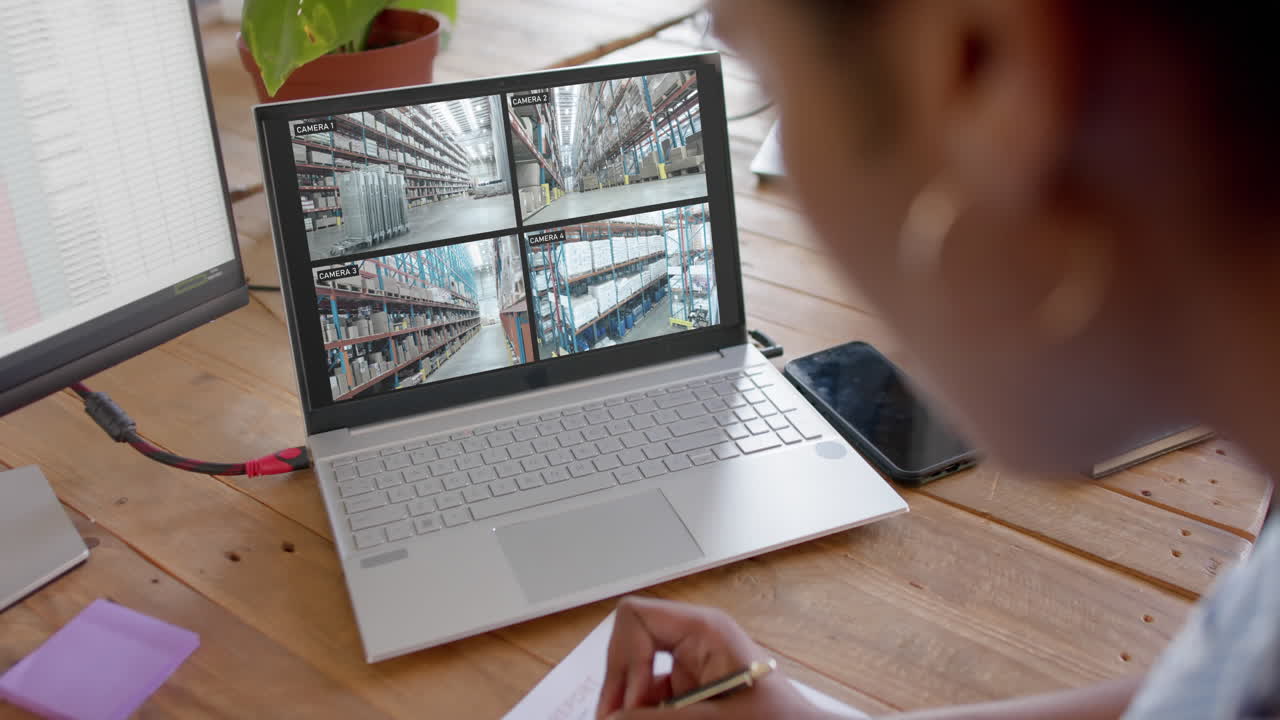 oficial de seguridad afroamericana viendo la cámara de cctv del almacén en la computadora portátil, en cámara lenta
