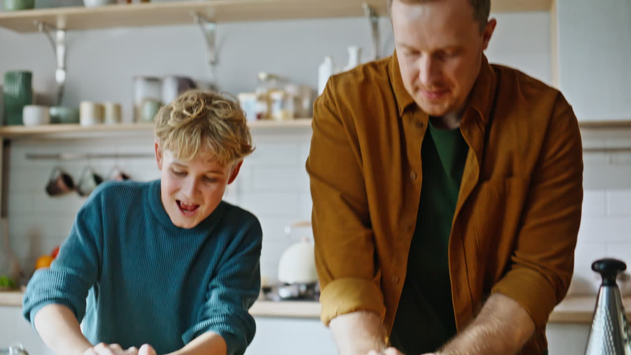 Vater-Sohn-Hände kneten Teig, Mehlzugebe auf Küchenarbeitsplatte, Nahaufnahme.