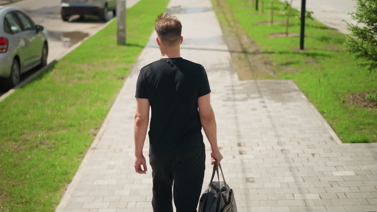 여유로운 개인이 시내 거리를 거닐고, 편안한 복장의 사람이 큰 가방을 들고 도시의 길을 따라 걷고, 격식 없는 옷차림의 느긋한 신사가 넉넉한 더플백을 들고 도시 거리를 다니고 있어요.