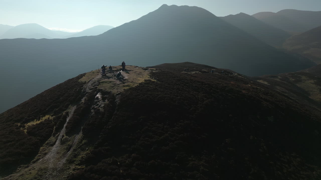 Hikers on hilltop with orbit revealing misty mountains and orange bracken at Barrow Fell English Lake District