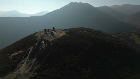 Hikers-on-hilltop-with-orbit-revealing-misty-mountains-and-orange-bracken-at-Barrow-Fell-English-Lake-District