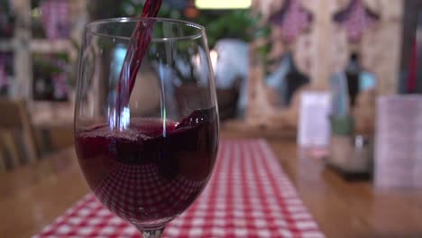 slow motion shot of a wine glass with red wine being poured in a restaurant