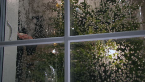 la mano de la mujer decora el árbol de navidad en un hogar cálido y acogedor, vista de la ventana desde el exterior