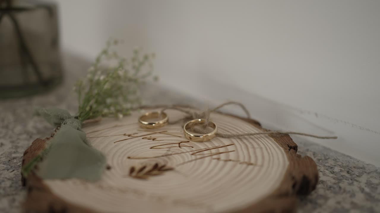 Close up of wedding rings on a wooden slab with greenery and baby's breath, creating a rustic and romantic detail