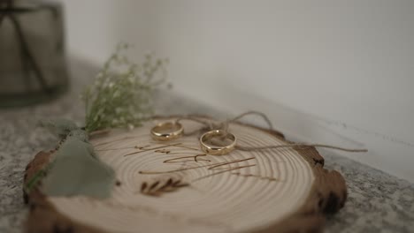 close up of wedding rings on a wooden slab with greenery and baby's breath, creating a rustic and romantic detail