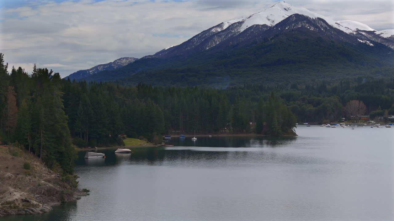 movimiento de drones de panorámica cerca de la orilla del lago de villa la angostura con montaña nevada, argentina.