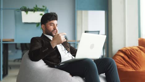 portrait-of-a-handsome,-stylish-young-man-of-Arab-descent-sitting-in-a-modern-office-of-a-business-center,-greeting-on-a-video-call-and-starting-a-conversation