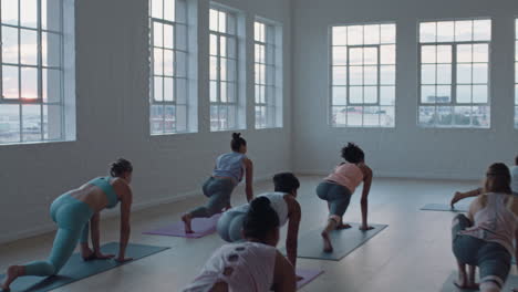 yoga class of healthy women practicing warrior pose enjoying exercising in fitness studio instructor leading group meditation teaching workout posture at sunrise