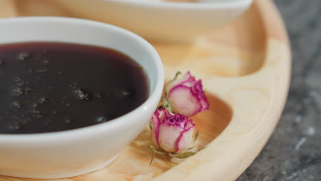 close-up of a white cup filled with honey, accompanied by powder tea and delicate dry flowers on a wooden tray, warm lighting enhances the natural textures