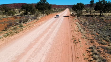 cinematic drone video from car driving on outback road in red sand with dust australia