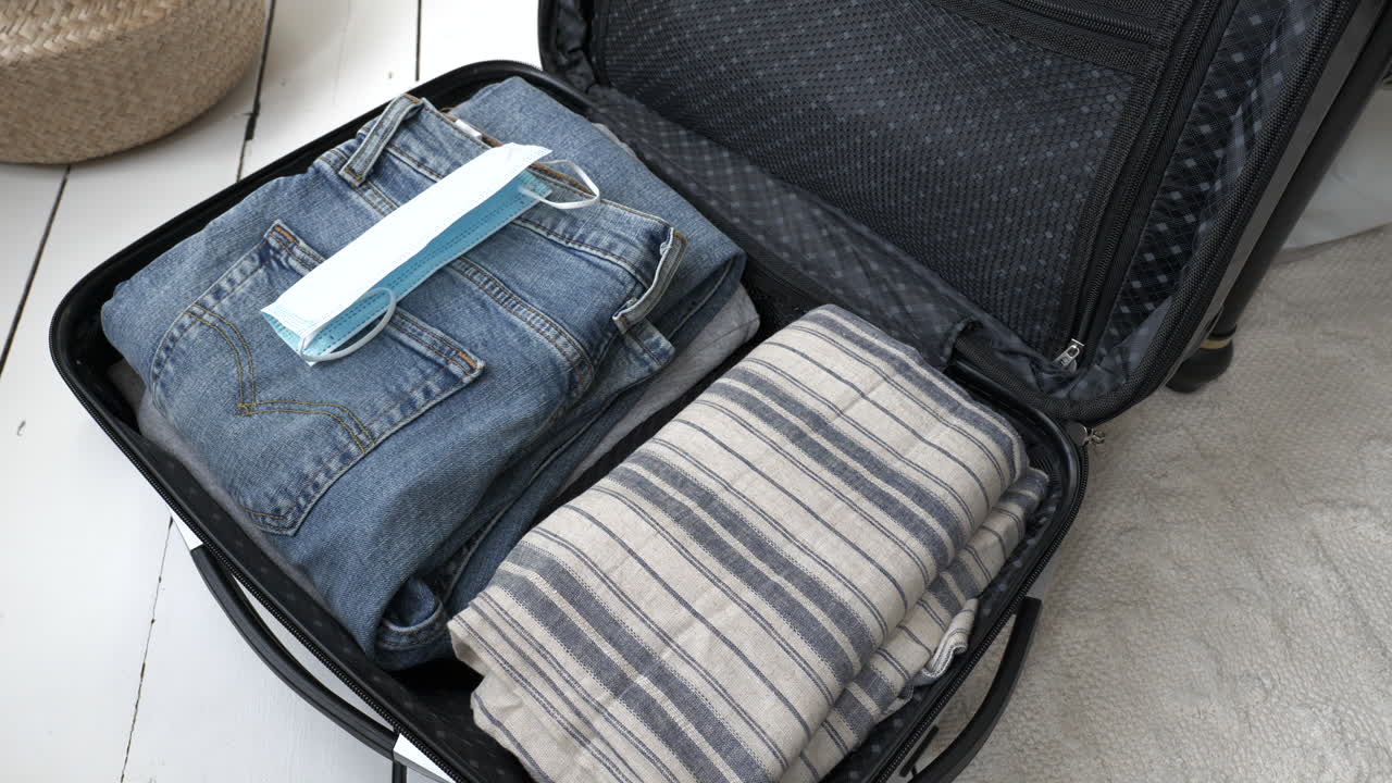 대유행 휴가를 위해 짐을 싸는 남자는 안면 마스크와 covid-19 테스트를 수하물에 포함합니다.