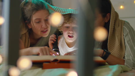 lesbian couple and little son reading book in bed