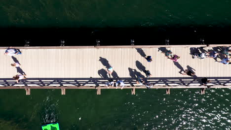 aerial: top down view of people walking on the wooden bridge in trakai with green color lake water visible in the background