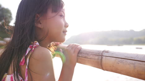 young girl looking at river from bamboo bridge