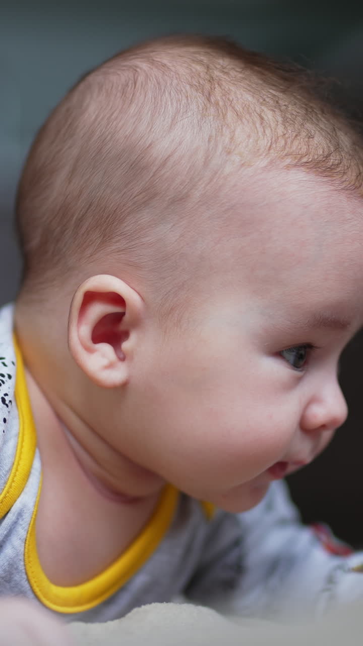Toddler boy stays up and tries to hold his head up. Cute little kid looking around. Close up. Blurred backdrop. Vertical video
