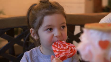 niño pequeño comiendo caramelo dulce en forma de corazón, cámara lenta. retrato de una niña lamendo una piruleta