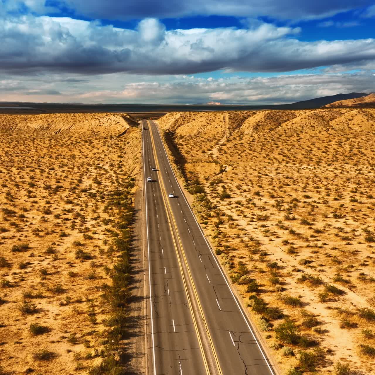 Drone moving above the four-lane highway in the dry desert. Arid landscape in California. Dramatic cloudscape in the sky at backdrop. Top view