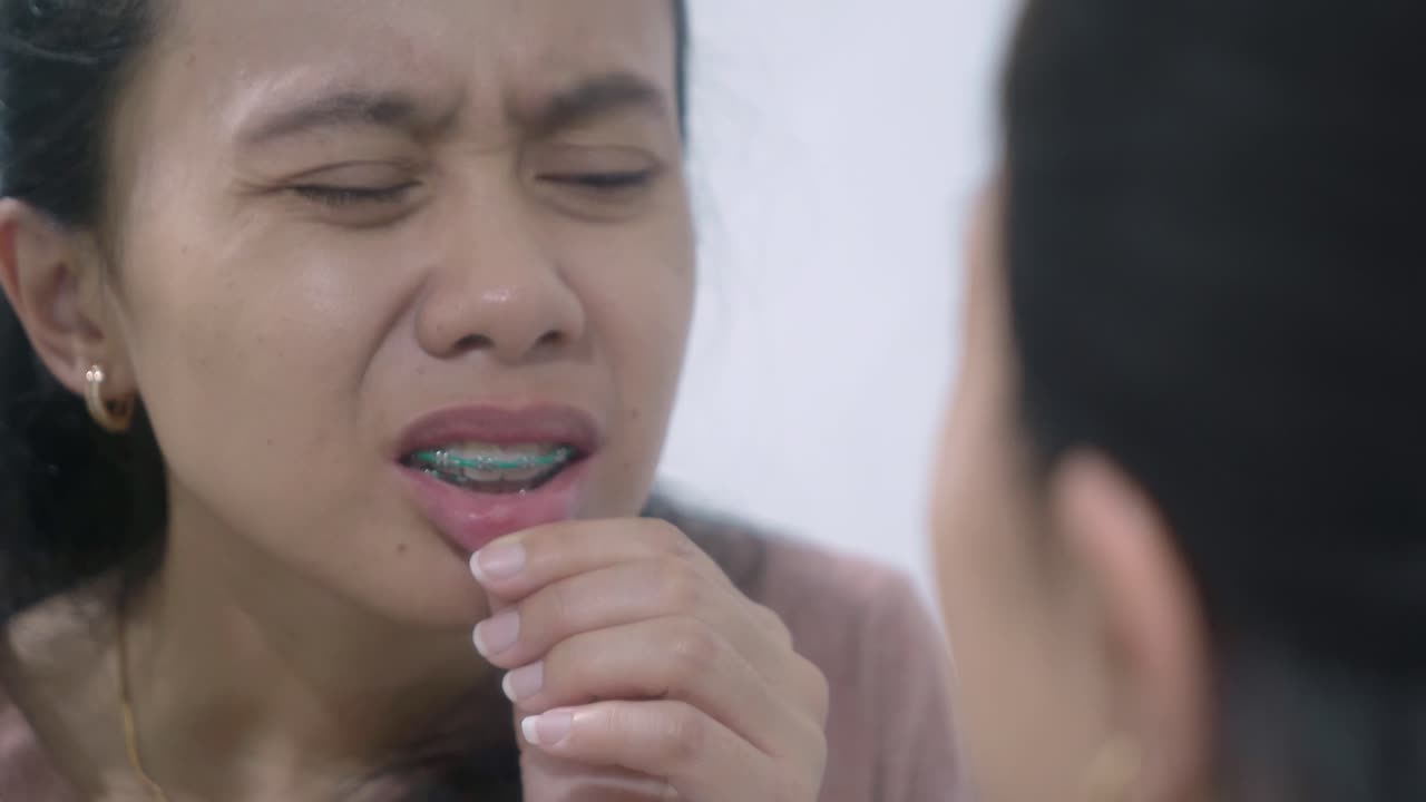 Woman with braces looking at her teeth in a mirror