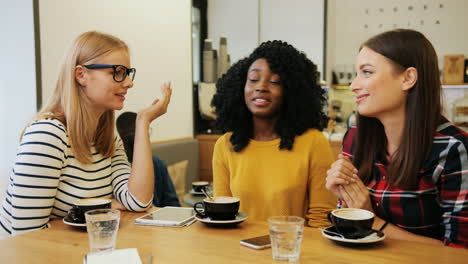 african american and caucasian women friends gossiping and laughing sitting at a table in a cafe