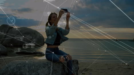 woman sitting on rock by sea with digital network animation overlay