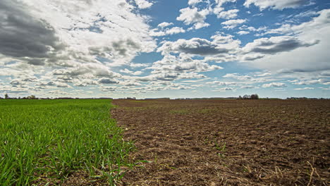 timelapse on farmland with half grass half dirt on a sunny day with moody clouds
