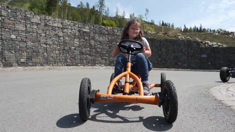 toma en cámara lenta de una niña pequeña en bicicleta en un cuadriciclo de pedal naranja en un resort privado en dolní morava, chequia, mientras otros niños andan en bicicleta detrás
