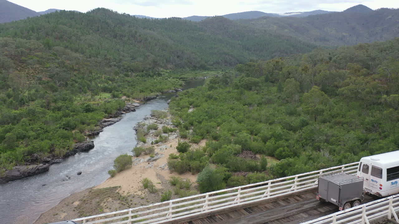 Aerial: Vans cross tall McKillops Bridge on Snowy River, VIC Australia