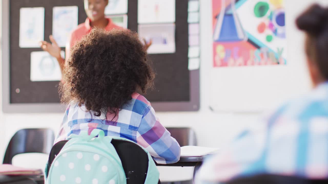 Portrait of diverse female teacher and happy schoolchildren at desks in school classroom