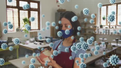 video compuesto de células de covid-19 flotando contra una alfarera que usa una máscara facial sosteniendo arcilla